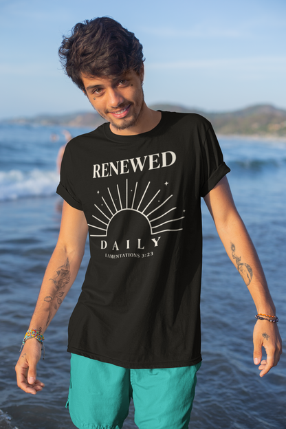 Man wearing a black t-shirt with 'RENEWED DAILY' text on a beach