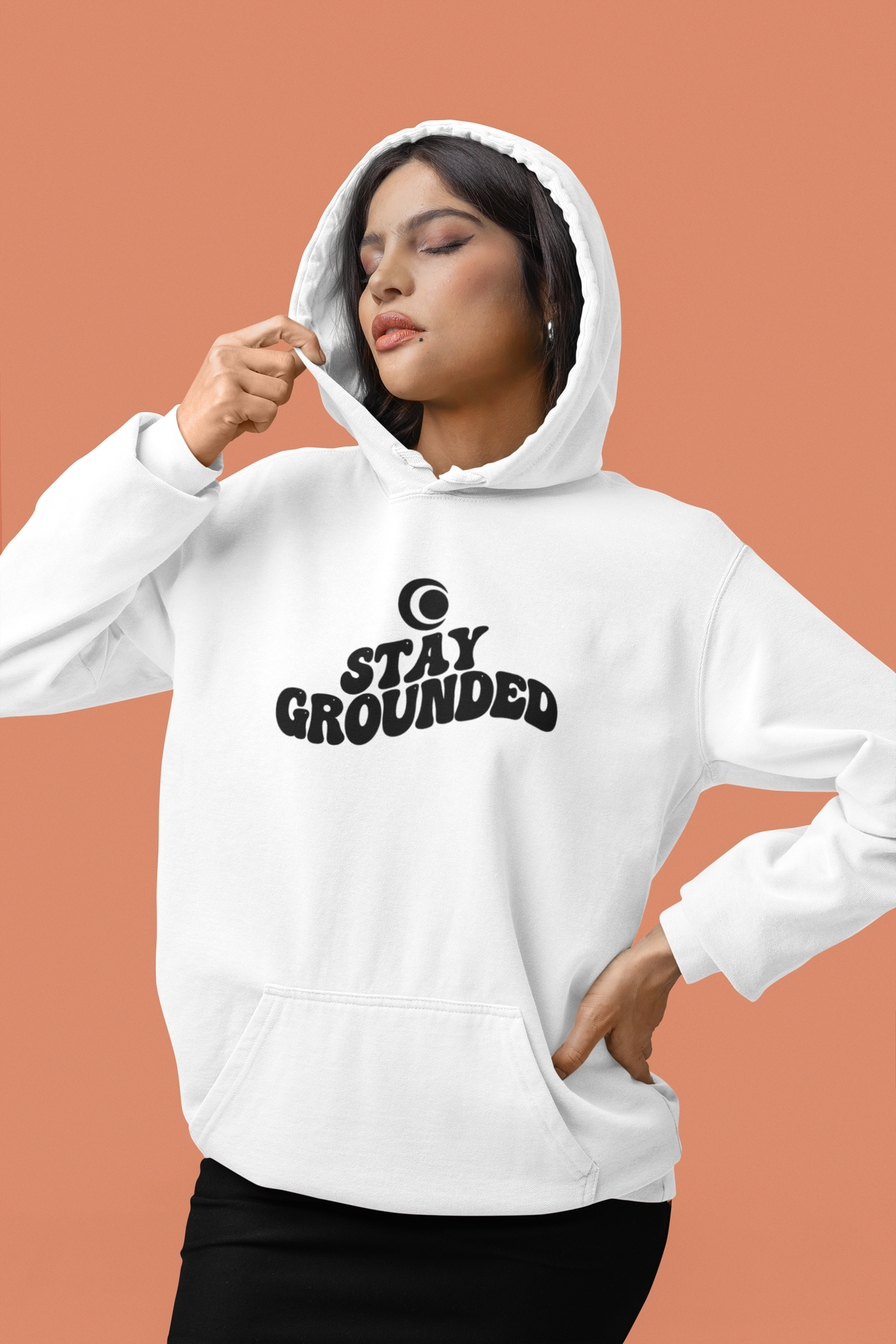 Person wearing a white hoodie with 'Stay Grounded' text on a peach background