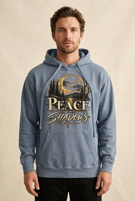  Model wearing a Blue Jean Peace in the Shadows hoodie with cream lettering, a golden crescent moon, moonlit water, woodland silhouettes, and a cross on the front.