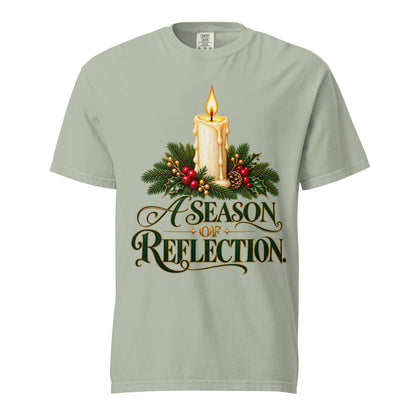 Man wearing an Ivory “A Season of Reflection” Christmas tee featuring a lit candle, evergreen branches, red berries, and green-and-gold lettering, paired with brown pants.