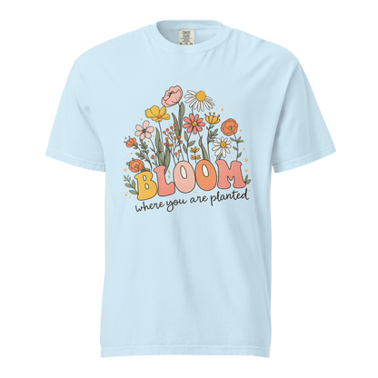 Flat mockup of a chambray (light blue) 'Bloom Where You Are Planted' garment-dyed tee with wildflower garden graphic.