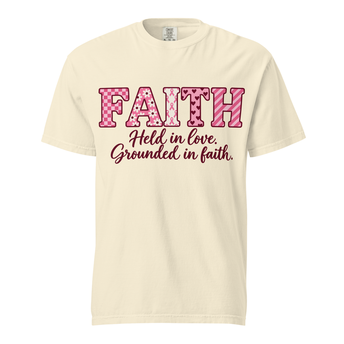  Ivory T-shirt with pink patterned FAITH lettering, awareness ribbon motifs, and burgundy “Held in love. Grounded in faith.” script.