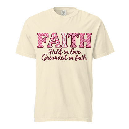  Ivory T-shirt with pink patterned FAITH lettering, awareness ribbon motifs, and burgundy “Held in love. Grounded in faith.” script.