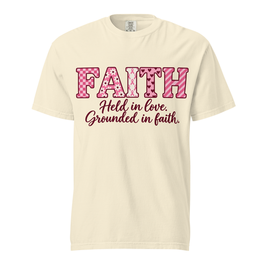  Ivory T-shirt with pink patterned FAITH lettering, awareness ribbon motifs, and burgundy “Held in love. Grounded in faith.” script.