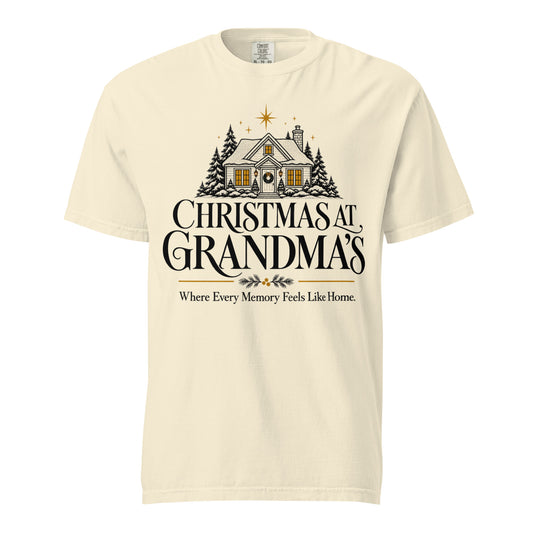 Front view of an Ivory “Christmas at Grandma’s” tee featuring a snowy cottage, evergreen trees, gold stars, and the words “Where Every Memory Feels Like Home.”