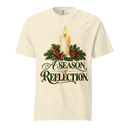 Front view of an Ivory “A Season of Reflection” Christmas tee featuring a lit candle, evergreen branches, red berries, a pinecone, and green-and-gold lettering.