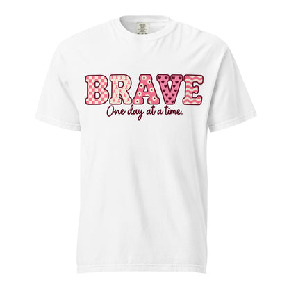 White T-shirt with pink patterned BRAVE lettering and burgundy “One day at a time” script on the front.
