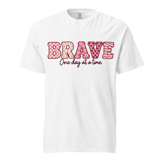 White T-shirt with pink patterned BRAVE lettering and burgundy “One day at a time” script on the front.
