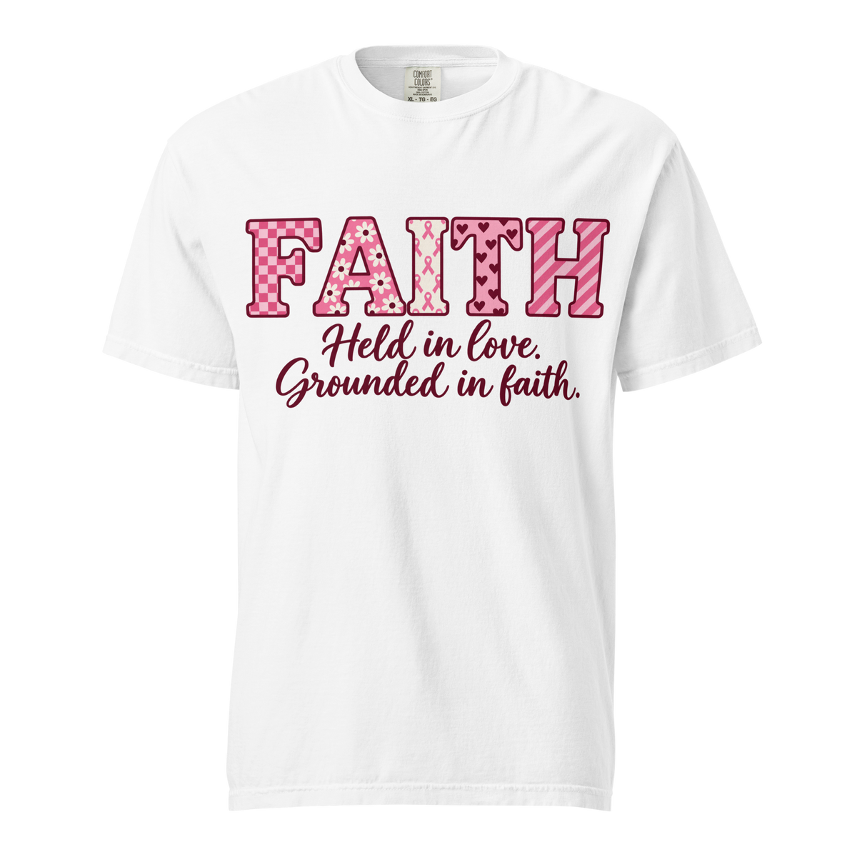 White T-shirt with pink patterned FAITH lettering, awareness ribbon motifs, and burgundy “Held in love. Grounded in faith.” script.