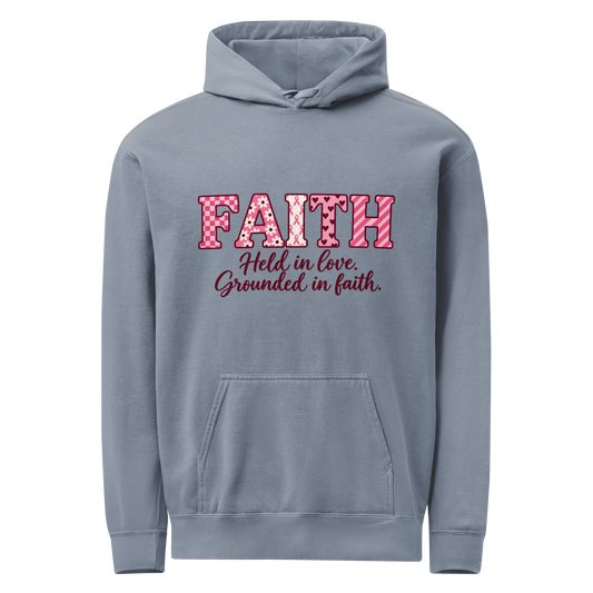 A Blue Jean hoodie with pink patterned FAITH lettering and “Held in love. Grounded in faith.” on the front