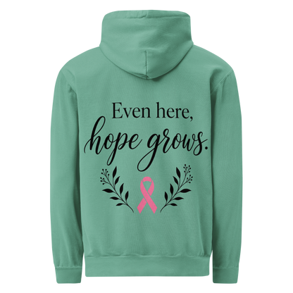 Seafoam hoodie back with black “Even here, hope grows.” lettering, a pink awareness ribbon, and botanical sprigs