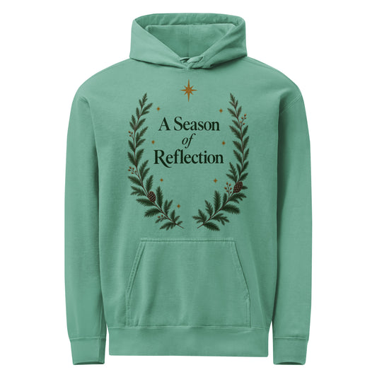 Front view of a seafoam A Season of Reflection hoodie with forest-green lettering, evergreen branches, pinecones and gold stars.