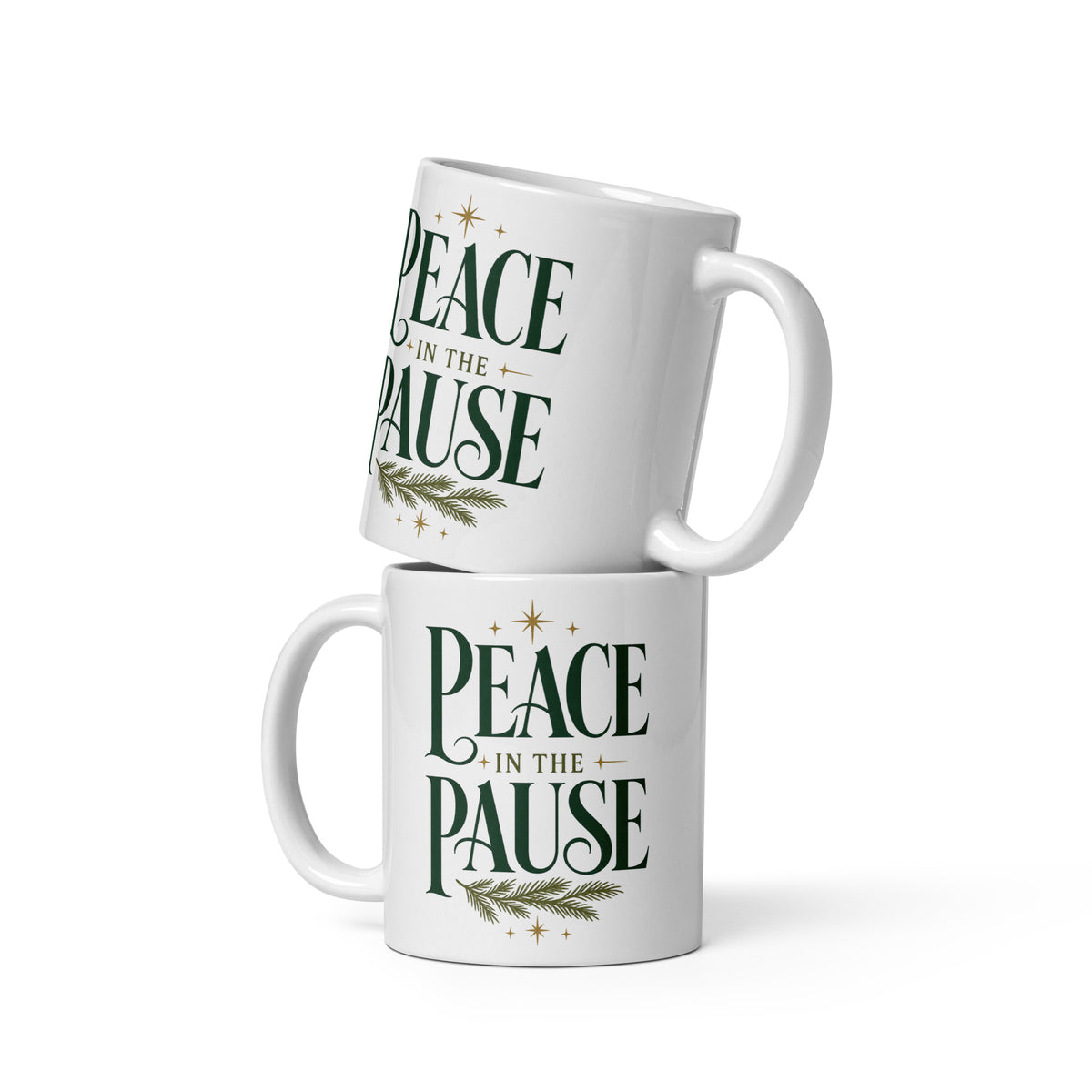Two white Peace in the Pause ceramic mugs stacked together, featuring forest-green lettering, gold stars, and an evergreen sprig.