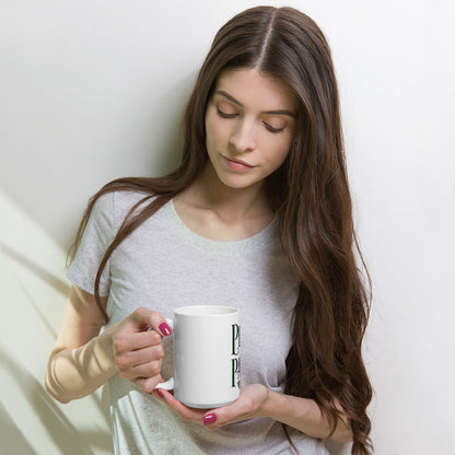 Woman holding a white 15 oz Peace in the Pause ceramic mug, with part of the forest-green lettering visible.